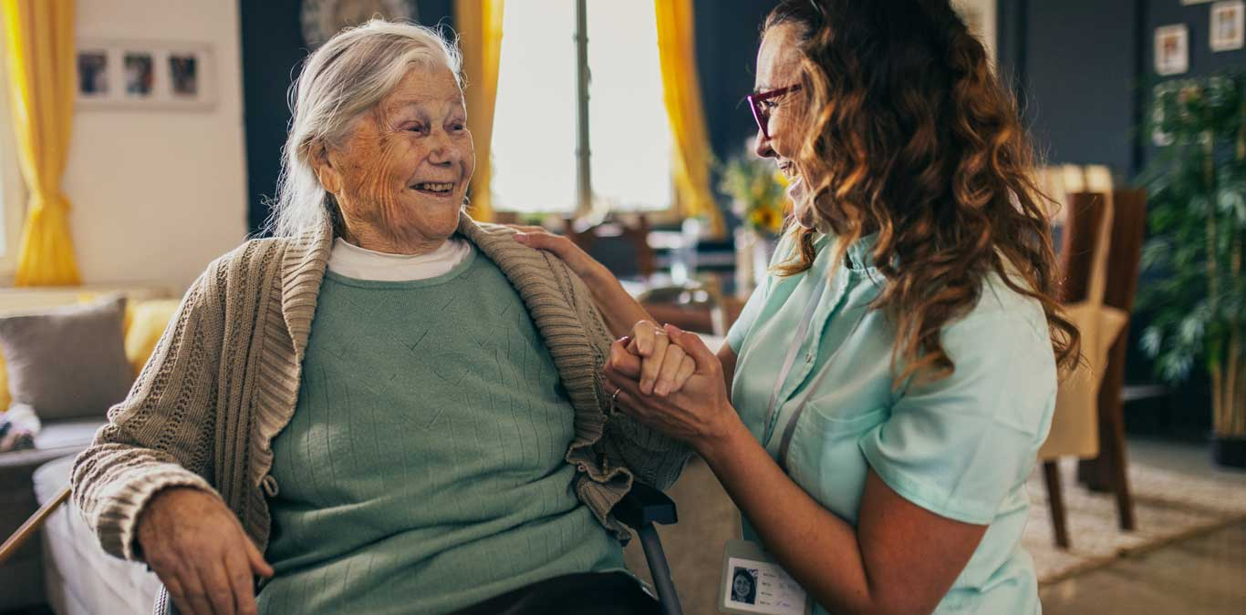 A hospice nurse visits with a smiling patient at home